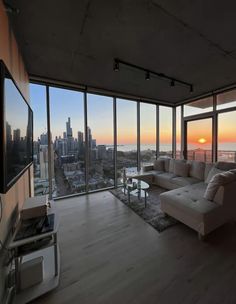 a living room filled with furniture and large windows overlooking the cityscape at sunset