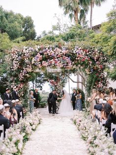 a couple getting married at their wedding under an archway with pink and white flowers on it