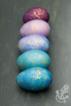 five colored eggs lined up in a row on a table with one painted purple, the other blue