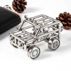 a silver car brooch sitting next to a wallet and pine cones on a white surface