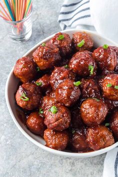 a white bowl filled with meatballs covered in sauce and garnished with parsley