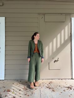 a woman standing in front of a garage door wearing green pants and a brown top