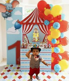 a little boy wearing a hat standing in front of a circus themed birthday cake stand