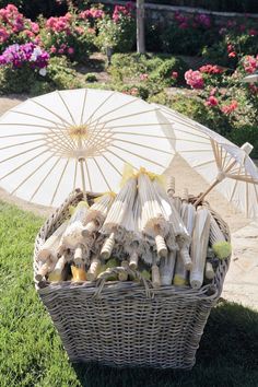 a wicker basket filled with garlic and an umbrella on top of green grass next to flowers