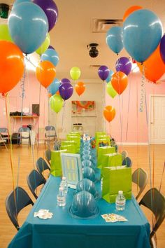 the table is set up for a party with colorful balloons and gift bags on it