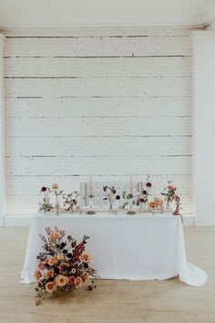 a table with flowers and candles on it in front of a white brick wall,