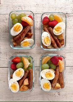 four glass containers filled with sausages, fruit and eggs on top of a wooden table