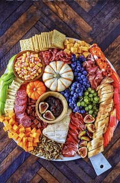 a platter filled with different types of cheeses, crackers and fruit on top of a wooden table