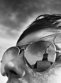 a man wearing sunglasses with the statue of liberty reflected in it