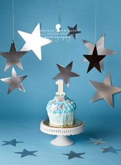 a cupcake with blue frosting and stars hanging from it's sides on a cake stand