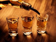 a person pouring whiskey into three glasses