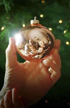 a person holding up a christmas ornament in front of a tree