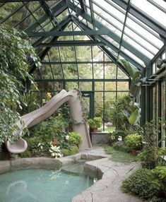 an indoor swimming pool with a slide in the center and plants around it, surrounded by greenery