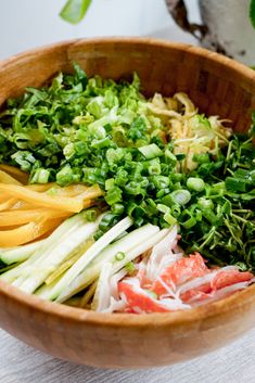 a wooden bowl filled with lots of different types of vegetables and herbs on top of a table