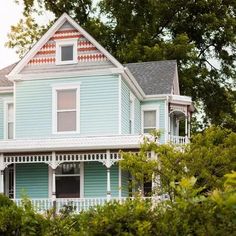 a blue house with white trim on the front and side of it, surrounded by trees