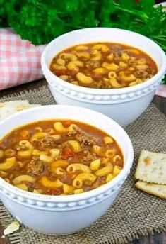 two white bowls filled with pasta and meat soup next to crackers on a table