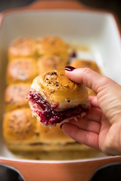 a hand holding a small sandwich with cranberry sauce on it in front of other muffins