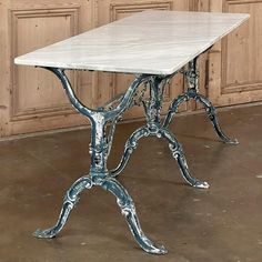 a white marble table with metal legs in front of wooden paneled walls and doors