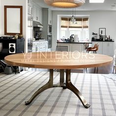 a round wooden table sitting in the middle of a living room next to a kitchen