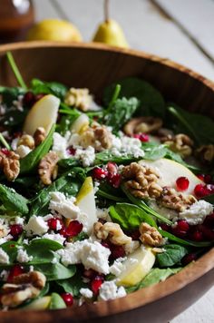 a wooden bowl filled with spinach, pears and feta cheese topped with walnuts