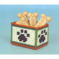 a crocheted dog treat box with four dogs in it and paw prints on the front