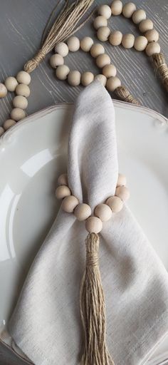 a white plate topped with a wooden bead and tasseled napkin on top of it