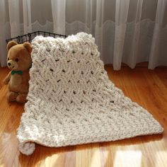 a teddy bear sitting on the floor next to a crocheted blanket