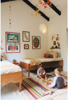 two small children playing on the floor in a room with white walls and wood beams