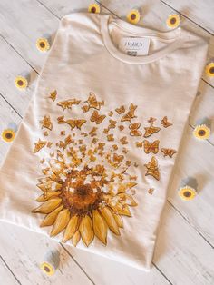 a white t - shirt with yellow butterflies and a sunflower in the center on a wooden floor