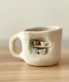 a ceramic cup with some plants and rocks on the inside is sitting on a table