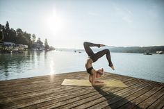 a woman doing a handstand on top of a wooden dock near the water