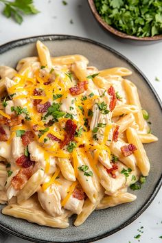 a pasta dish with chicken, bacon and cheese on a plate next to a bowl of parsley