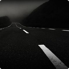 an empty road in the middle of a forest at night with fog on the trees