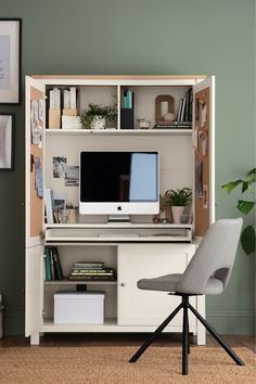 a desk with a computer on it and a chair next to it in front of a green wall