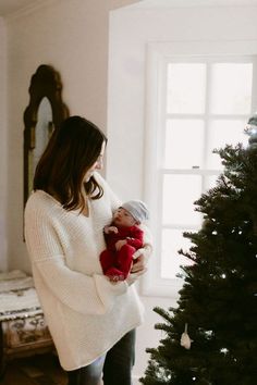 a woman holding a baby next to a christmas tree