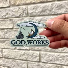 someone is holding up a sticker that says god works on the side of a brick wall