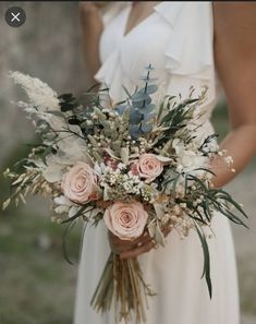 a woman in a white dress holding a bouquet of flowers and greenery on her wedding day