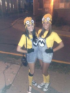 two women dressed in minion costumes standing next to each other on the sidewalk at night