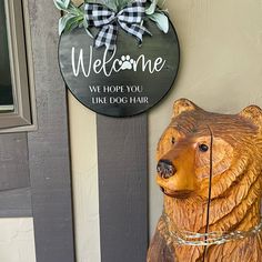 a wooden bear statue sitting next to a welcome sign on a door way that says, we hope you like dog hair