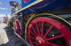 an old fashioned train is parked on the side of the road with flags flying in the wind