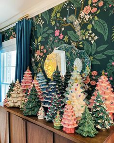 colorful christmas trees are lined up on a shelf in front of a wallpapered room