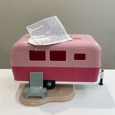 a pink toy camper with a little chair on the side and a piece of paper stuck to it