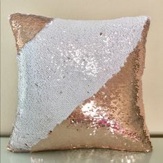 a white and gold pillow with sequins on it sitting on a table next to a wall