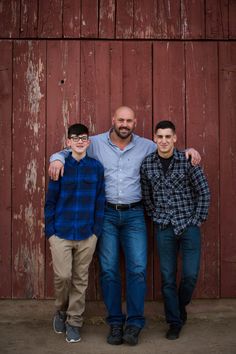 three men standing next to each other in front of a wooden wall