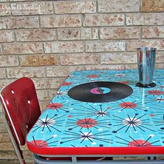 a table with a record on it next to a red metal chair and brick wall