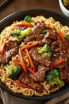 beef, broccoli and carrots are served with noodles on a black plate