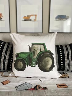 a green tractor pillow sitting on top of a bed next to two black and white pillows