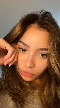 a woman with long brown hair is holding her hand on her head and looking at the camera