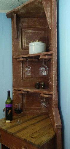 an old wooden shelf with wine glasses and a bottle on the table next to it