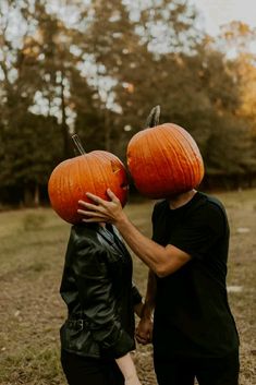 two people with pumpkins on their heads walking through the grass together in front of trees